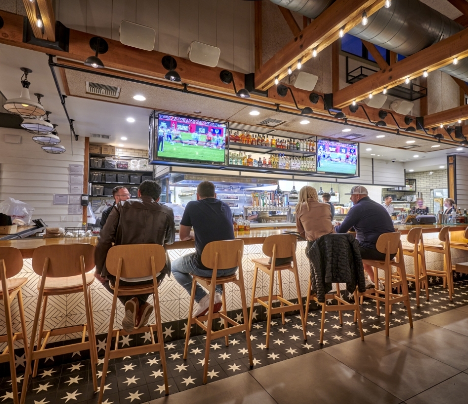 Customers seated at a trendy bar inside Wood Ranch BBQ & Grill, enjoying the vibrant atmosphere with star-patterned bar chairs and a contemporary design.