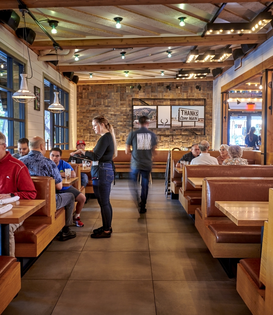 Guests dining inside Wood Ranch BBQ & Grill with a relaxed vibe, surrounded by rustic wooden décor and a homely atmosphere enhanced by string lights.
