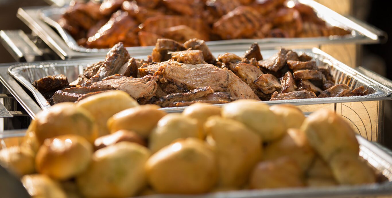 Buffet trays filled with succulent slices of brisket and chicken, accompanied by a pile of glossy buns in the foreground, all bathed in warm sunlight.
